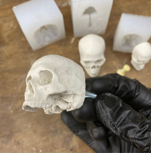 Skull-shaped mold held by a gloved hand with silicone molds in the background.