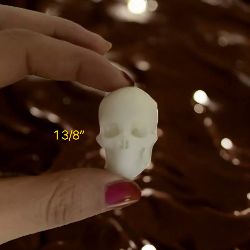 Hand holding a small skull-shaped object with measurement '13/8"' against a blurred background.