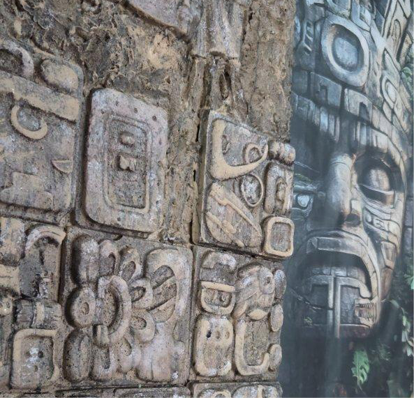 Close-up of ancient stone carvings with intricate designs and a large mask-like figure in the background.