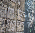 Close-up of ancient stone carvings with intricate designs and a large mask-like figure in the background.