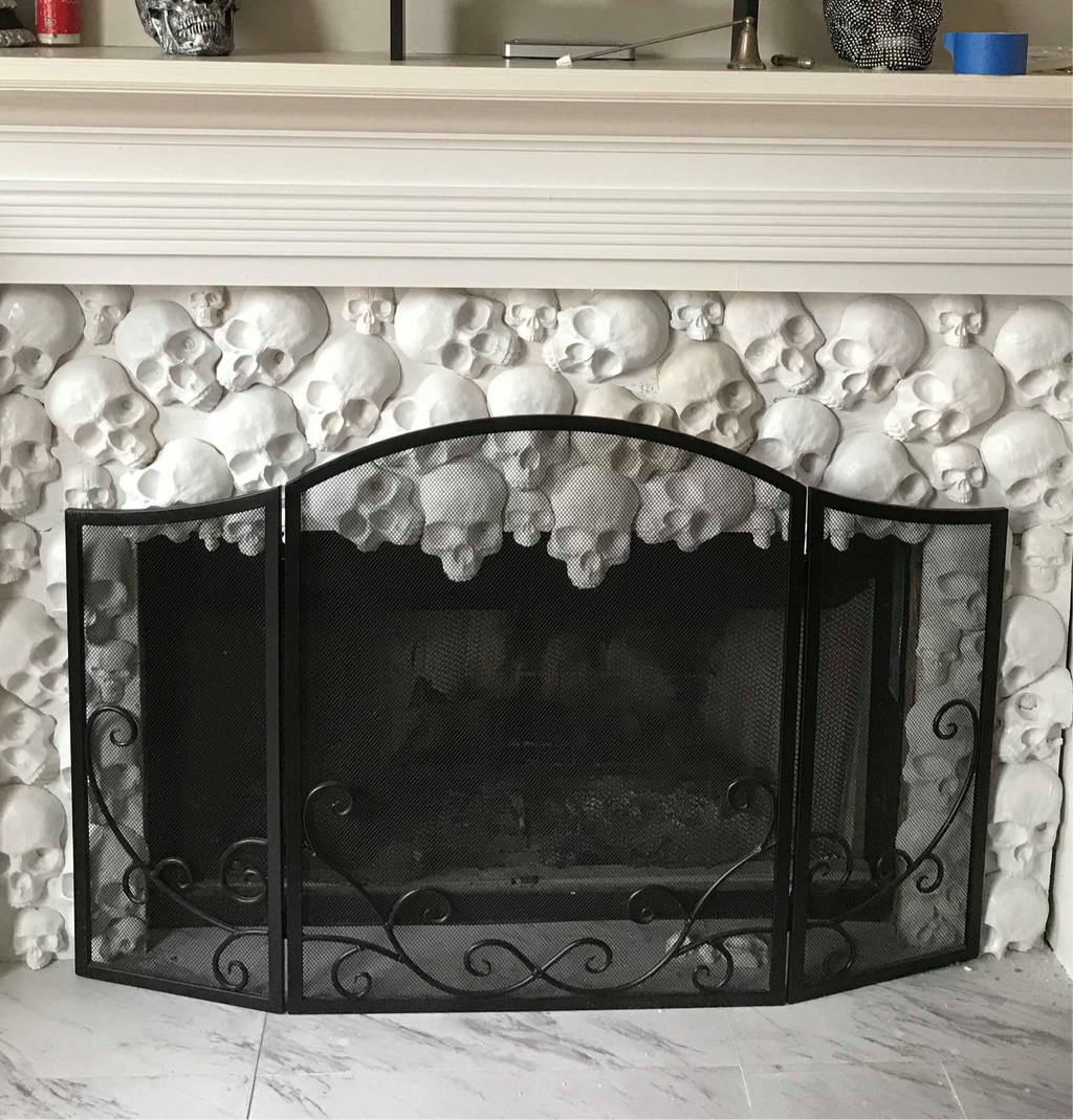 Set of white plaster skull castings arranged decoratively around a fireplace with black metal screen, showing finished results from Pacific Mold Design skull fireplace mold set