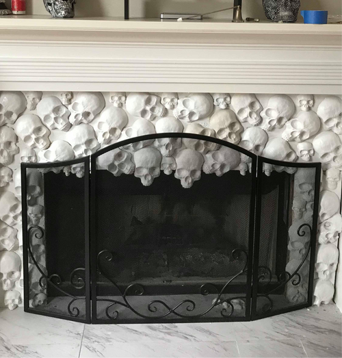Set of white plaster skull castings arranged decoratively around a fireplace with black metal screen, showing finished results from Pacific Mold Design skull fireplace mold set