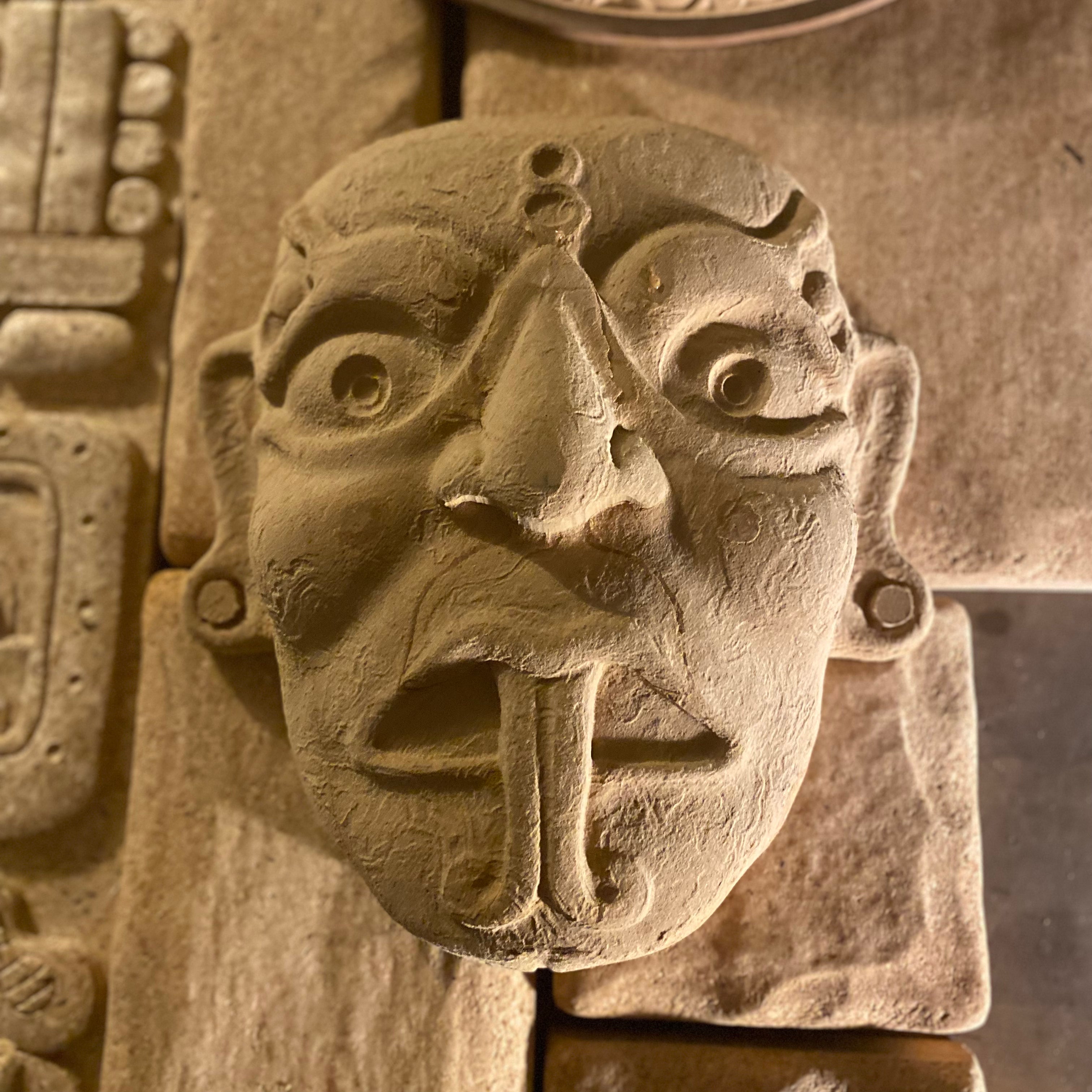 A stone carving of a Mayan serpent deity face.